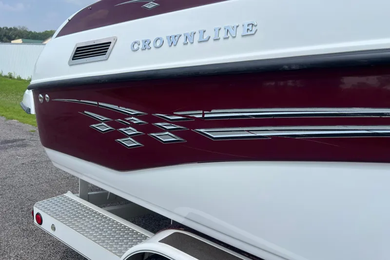 Slide: The Image of 2003 Crownline 230 BR boat with maroon and white design, parked on a trailer. - 14