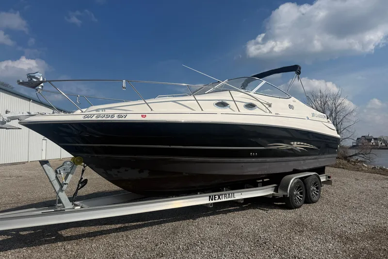 The Image of 2007 Larson Cabrio 260 boat on trailer, parked outdoors under a clear sky. - 0