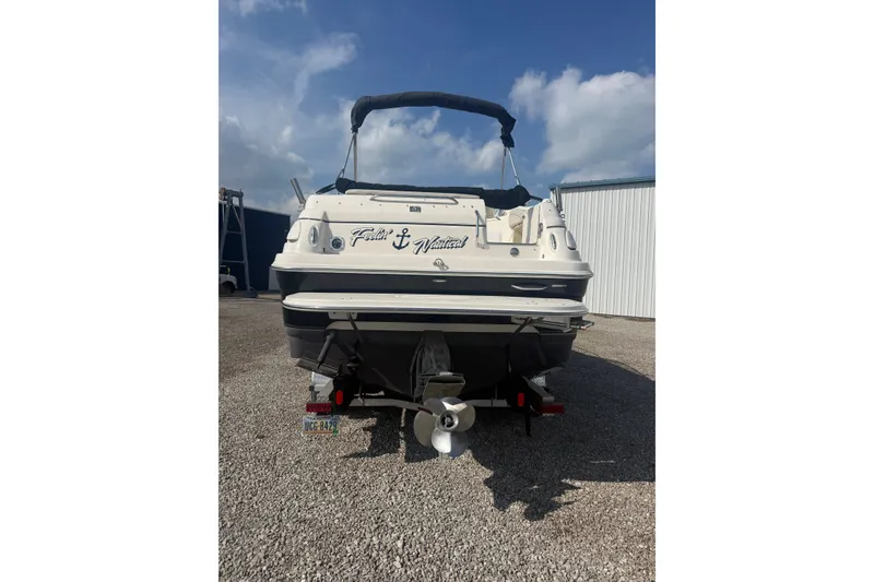 Slide: The Image of 2007 Larson Cabrio 260 boat rear view, parked on gravel, under a clear blue sky. - 22