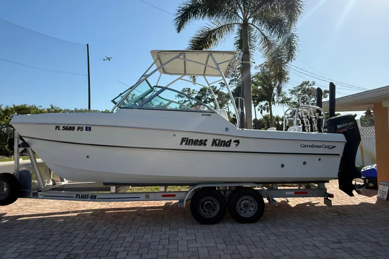 The Image of 2014 Carolina Cat 23DC boat on trailer, labeled "Finest Kind," parked near palm trees. - 0