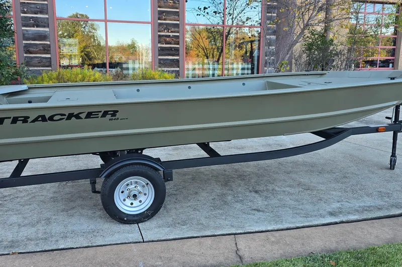 Slide: The Image of 2026 Tracker Grizzly 1648 Utility boat on trailer, parked outdoors near a building. - 2