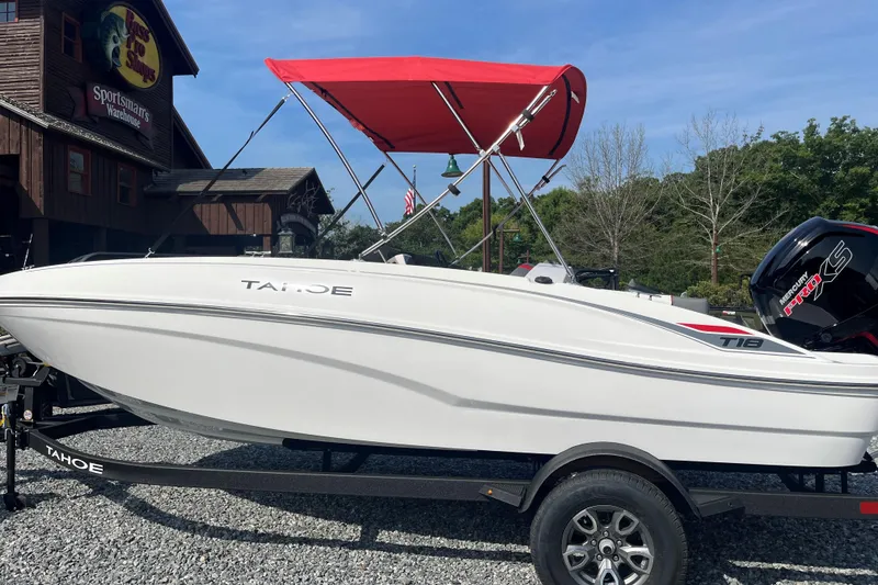 The Image of 2026 Tahoe T18 boat with red canopy on trailer outside a warehouse. - 0