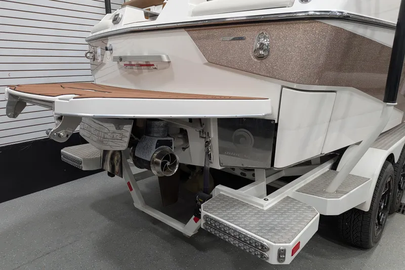 Slide: The Image of 2021 Malibu M240 boat rear view with swim platform and trailer in showroom. - 13