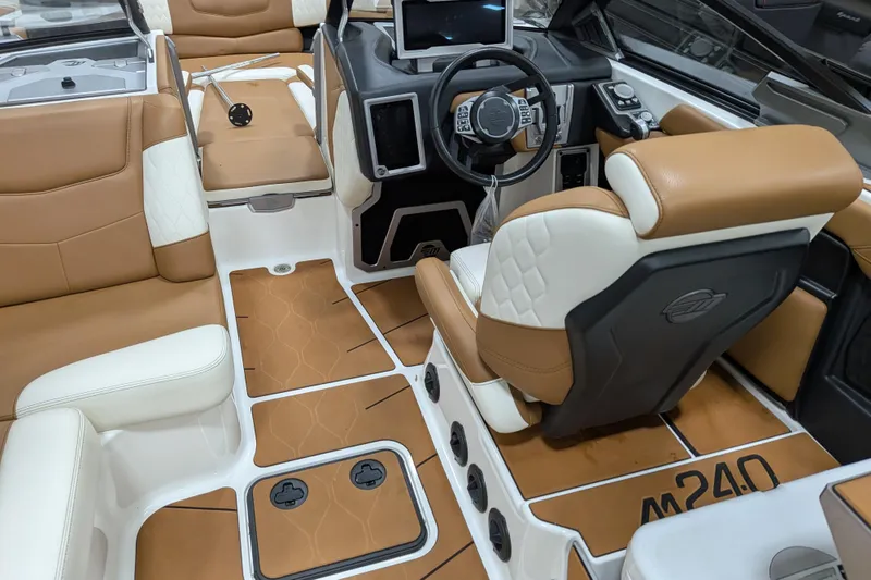 Slide: The Image of 2021 Malibu M240 boat interior with tan and white seating, modern dashboard, and steering wheel. - 21