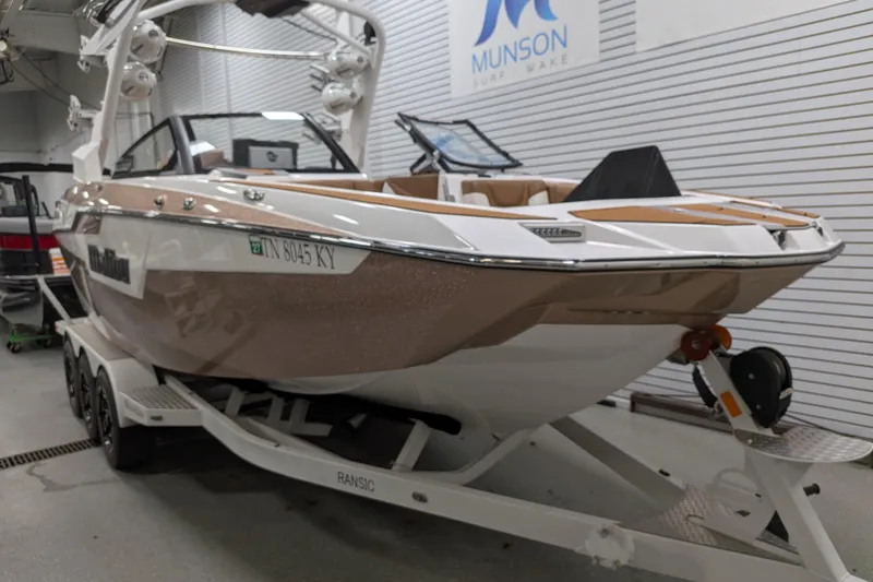 Slide: The Image of 2021 Malibu M240 boat on trailer in showroom, Munson Surf Wake sign visible. - 3
