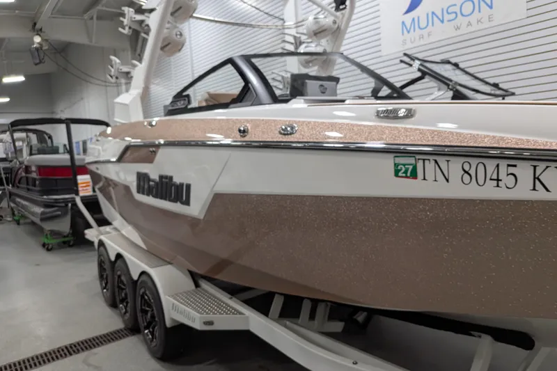 Slide: The Image of 2021 Malibu M240 boat in showroom, featuring sleek design and triple-axle trailer. - 4