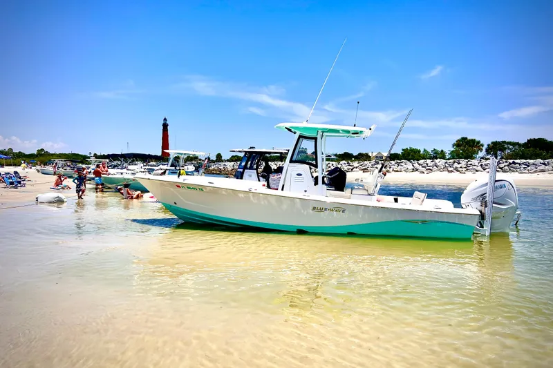 The Image of 2022 Blue Wave 2800 Pure Hybrid boat anchored on a sunny beach with lighthouse in background. - 0