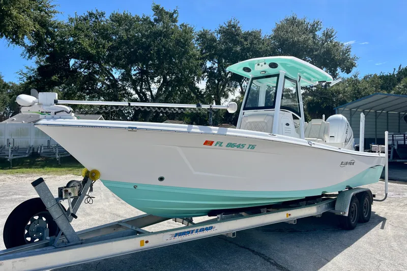 Slide: The Image of 2022 Blue Wave 2800 Pure Hybrid boat on trailer, parked outdoors. - 2