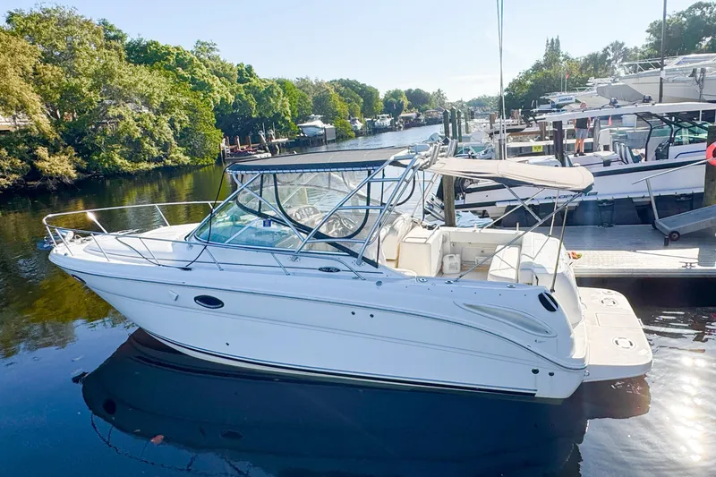 The Image of 2006 Sea Ray 290 Amberjack boat docked on a serene river with lush greenery. - 0