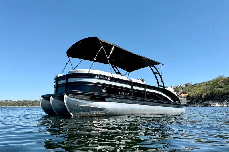 The Image of 2022 Harris Sunliner 250 pontoon boat on a sunny lake, featuring sleek design and canopy. - 1