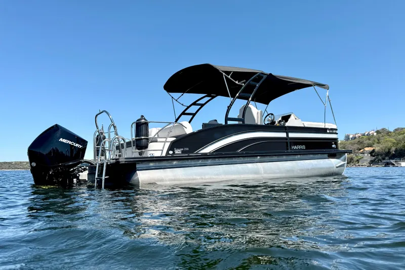 Slide: The Image of 2022 Harris Sunliner 250 pontoon boat on water, featuring a sleek black design. - 5