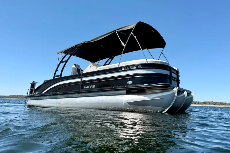 Slide: The Image of 2022 Harris Sunliner 250 pontoon boat on calm water under clear blue sky. - 7