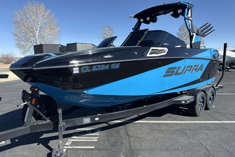 The Image of 2021 Supra SA 450 boat in blue and black on a trailer in a parking lot. - 1