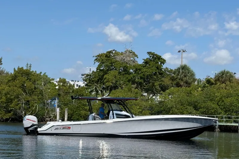 Slide: The Image of 2018 Nor-Tech 390 Sport Center Console boat on calm water, surrounded by lush greenery. - 7