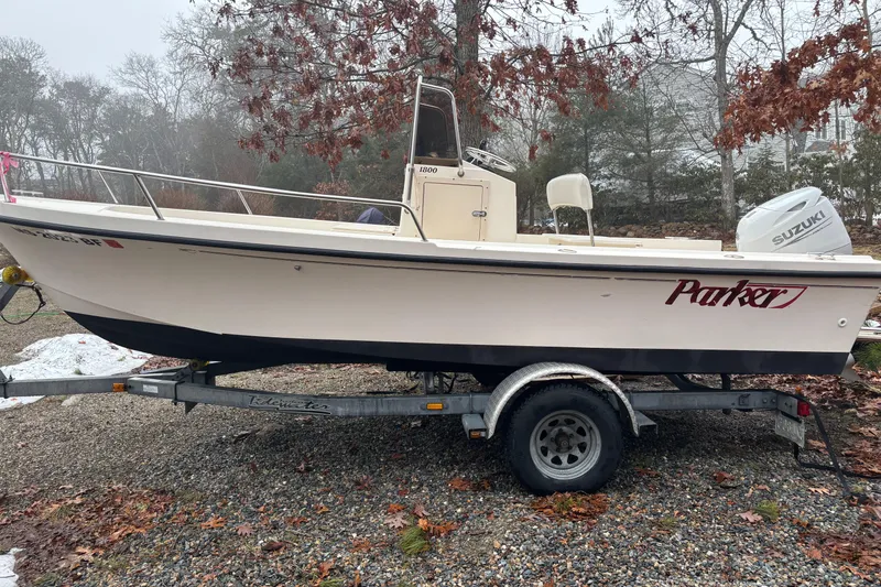 The Image of 1998 Parker 1801 Center Console boat on trailer, parked outdoors with Suzuki engine. - 1