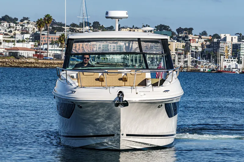 Slide: The Image of 2023 Sea Ray Sundancer 320 OB cruising in a marina with cityscape background. - 2