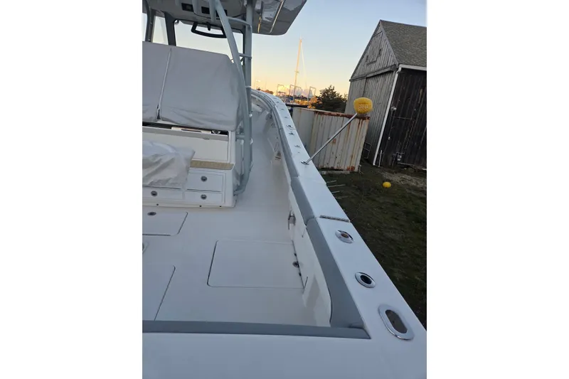 Slide: The Image of 2019 Regulator 41 boat deck with seating and storage, docked near a rustic building. - 20