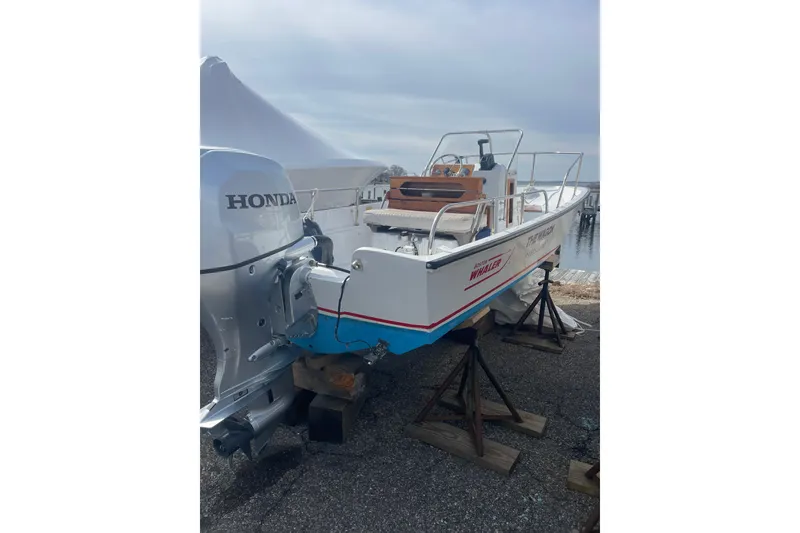 The Image of 1987 Boston Whaler 17 Montauk boat with Honda outboard motor on stands by the water. - 0