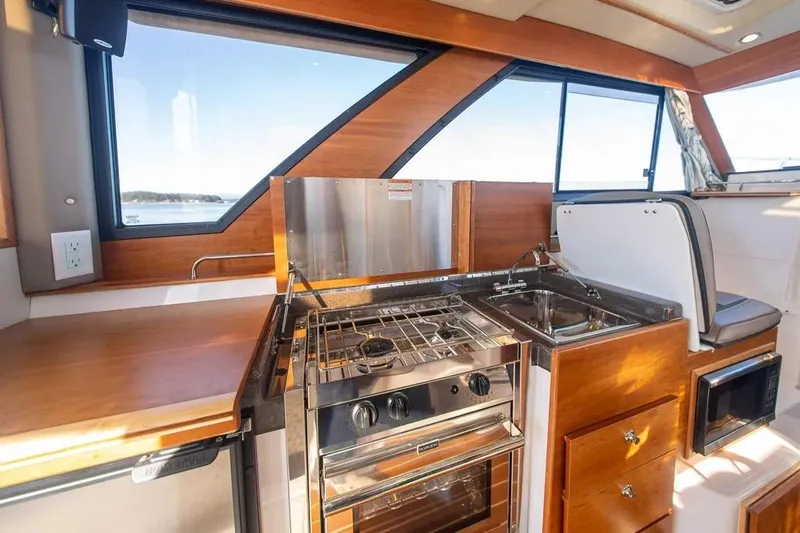 Slide: The Image of 2023 Cutwater C-32 Coupe interior kitchen with stove, sink, and wooden cabinetry. - 33