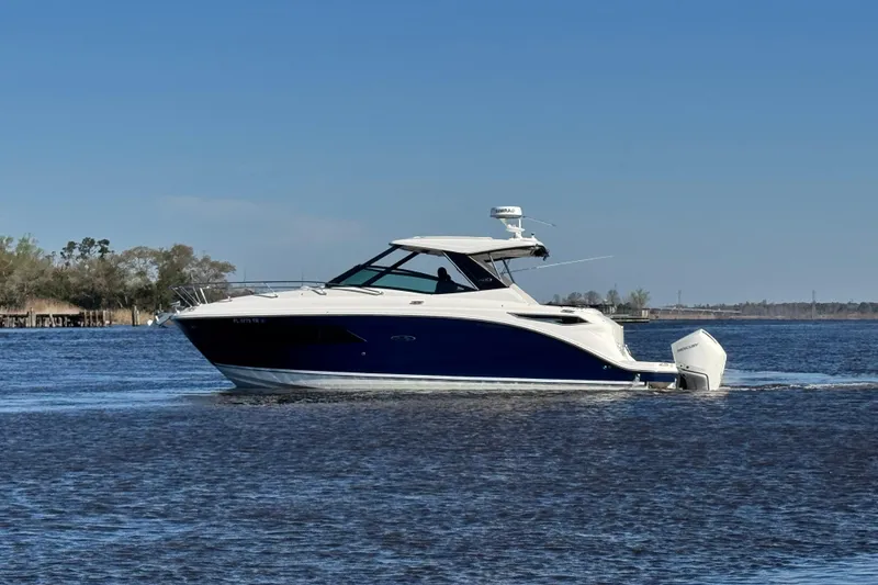 Slide: The Image of 2024 Sea Ray Sundancer 320 Outboard cruising on a calm lake under a clear blue sky. - 10
