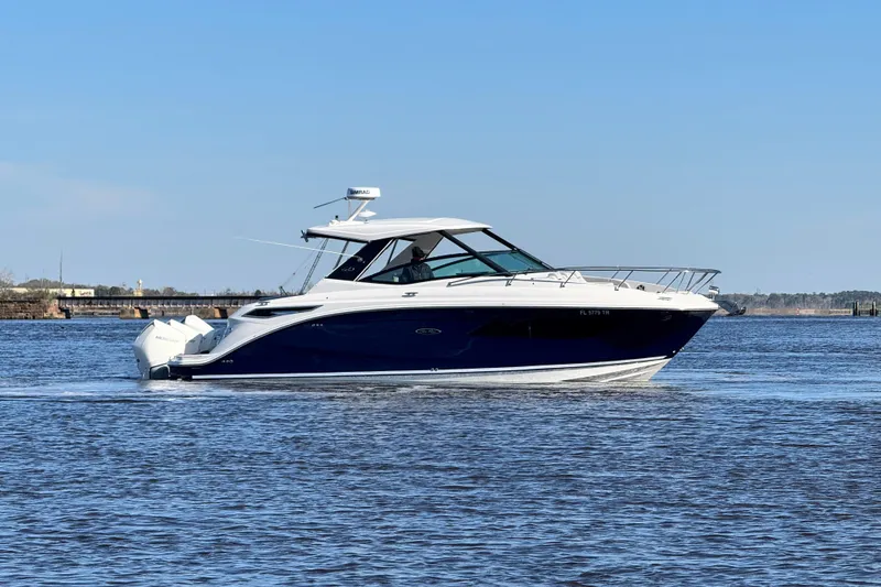 Slide: The Image of 2024 Sea Ray Sundancer 320 Outboard cruising on a calm waterway under a clear blue sky. - 11