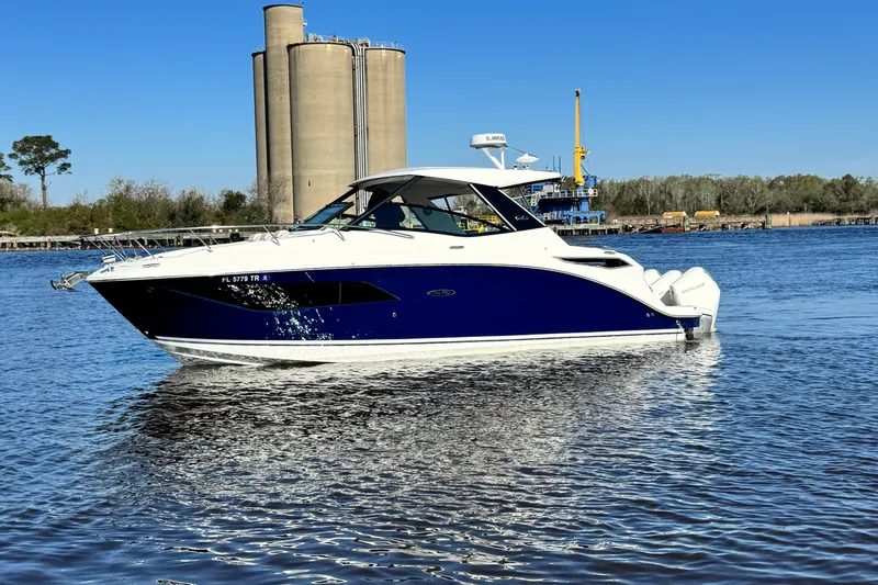 Slide: The Image of 2024 Sea Ray Sundancer 320 Outboard cruising on a calm river with industrial backdrop. - 12