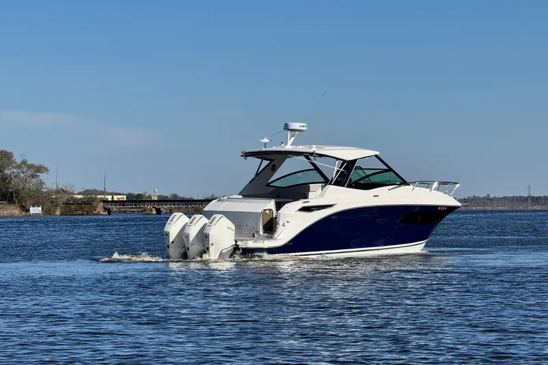Slide: The Image of 2024 Sea Ray Sundancer 320 Outboard cruising on a calm lake under a clear blue sky. - 2