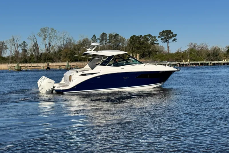 Slide: The Image of 2024 Sea Ray Sundancer 320 Outboard cruising on a calm river under clear blue skies. - 4