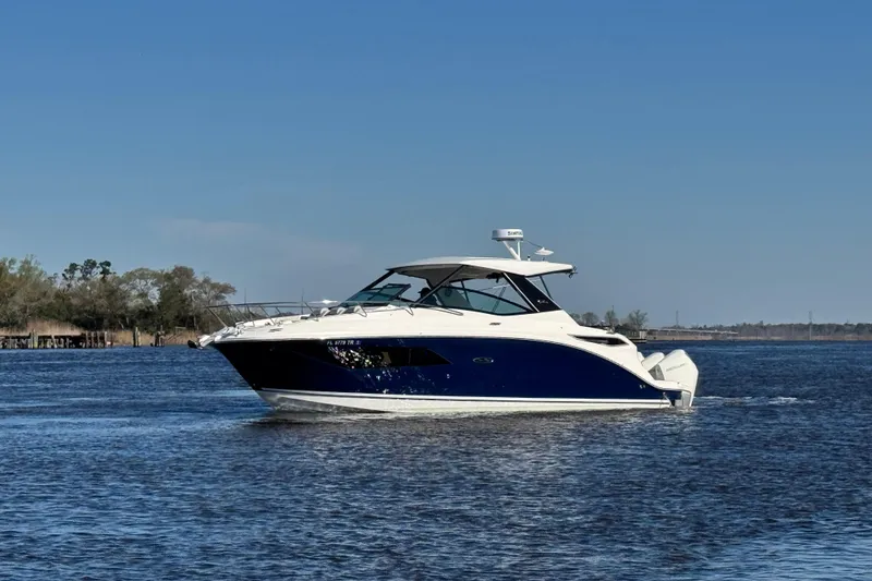 Slide: The Image of 2024 Sea Ray Sundancer 320 Outboard cruising on a calm lake under a clear blue sky. - 8