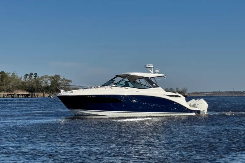 Slide: The Image of 2024 Sea Ray Sundancer 320 Outboard cruising on a calm lake under a clear blue sky. - 9