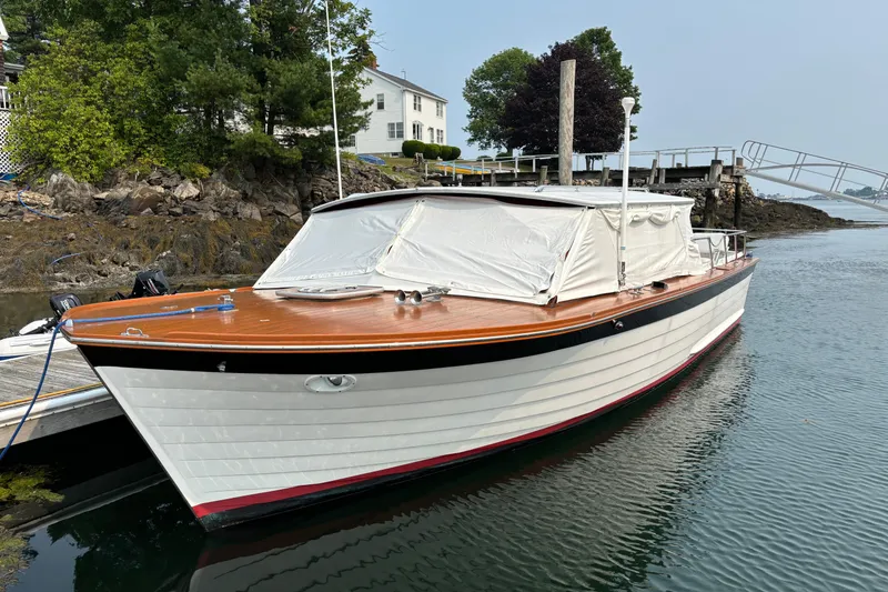 Slide: The Image of 1967 Lyman Islander 30 boat docked by rocky shoreline with trees and house. - 10