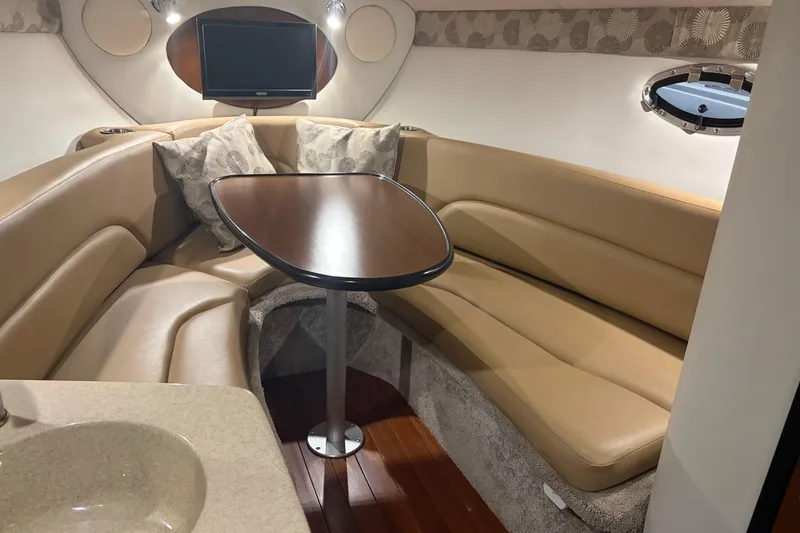 Slide: The Image of 2021 Crownline 264 CR cabin interior with beige seating, wooden table, and mounted TV. - 26