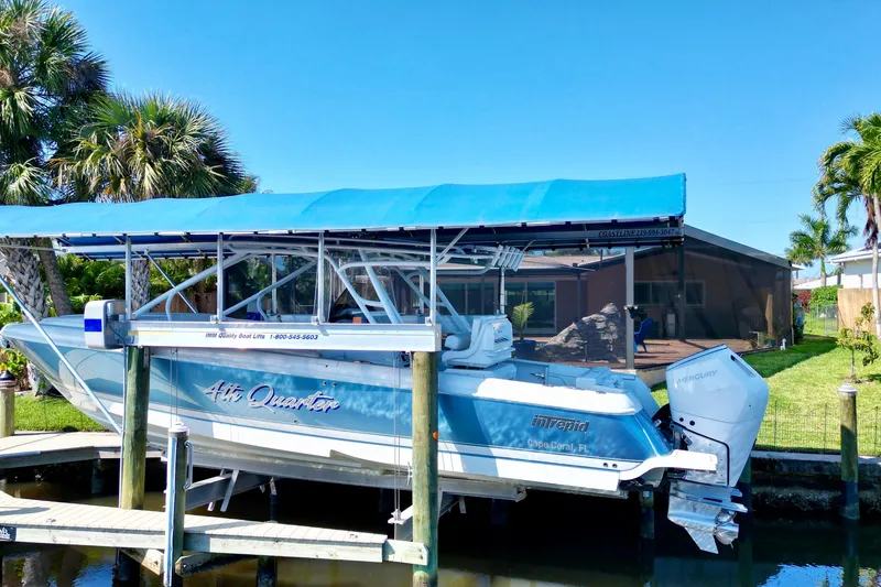 Slide: The Image of 2025 Intrepid 327 Cuddy boat docked with blue canopy, surrounded by palm trees. - 37