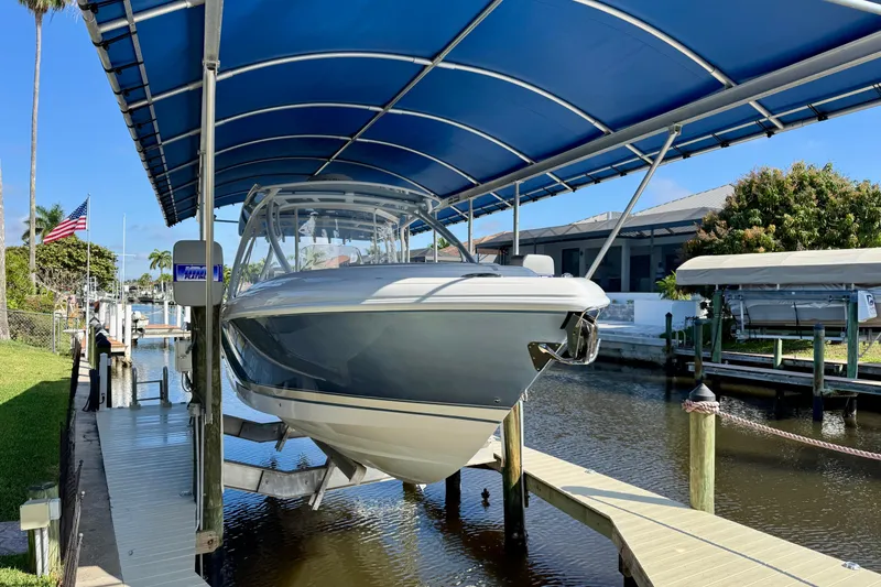 Slide: The Image of 2025 Intrepid 327 Cuddy boat docked under blue canopy in sunny marina. - 6