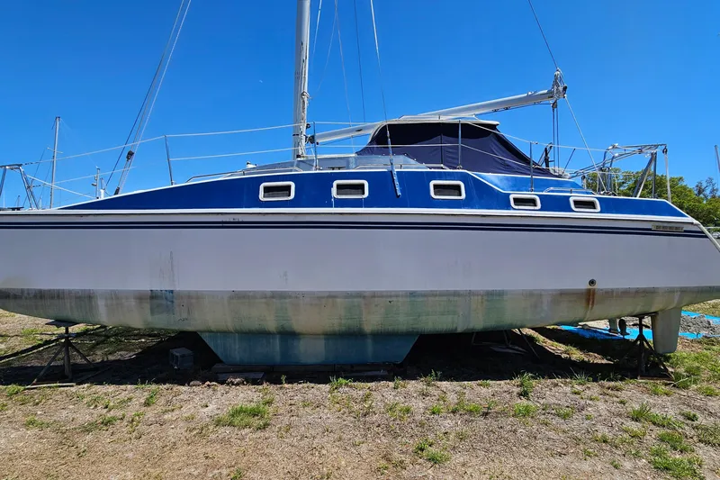 Slide: The Image of Sailboat PDQ 32 LRC 1996 on land, blue and white hull, clear sky background. - 34