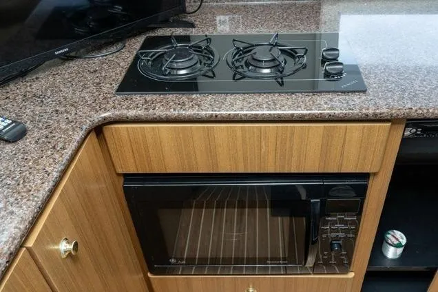 Slide: The Image of 2002 Bayliner 3488 Avanti kitchen with stove and microwave, featuring wood cabinetry. - 12