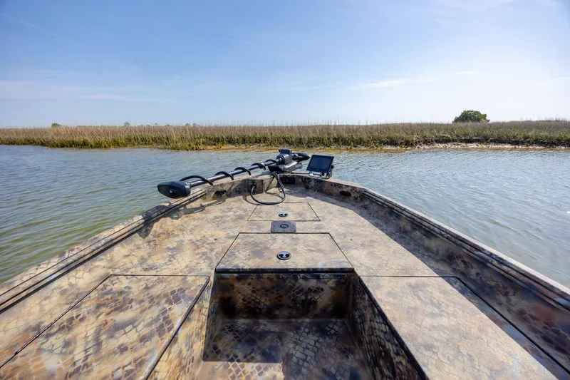 Slide: The Image of 2026 Excel 203 Bay Pro Elite boat on calm water near grassy shoreline. - 10