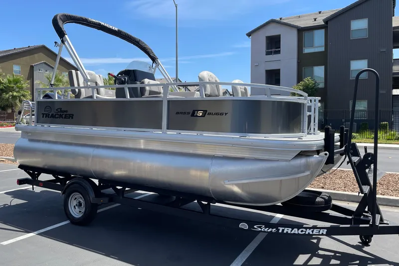 Slide: The Image of 2026 Sun Tracker Bass Buggy 16 XL Select pontoon boat on trailer in parking lot. - 2
