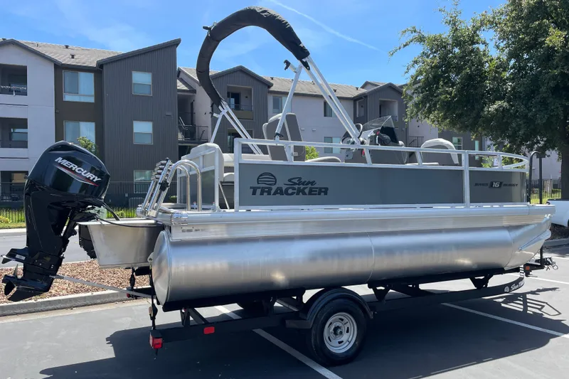 Slide: The Image of A Sun Tracker Bass Buggy 16 XL Select pontoon boat on a trailer in a residential area. - 3