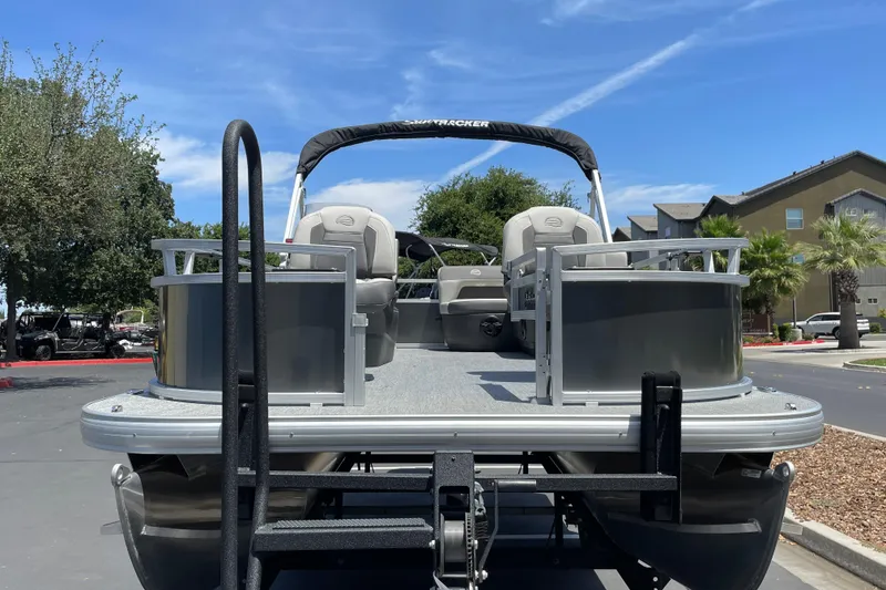 Slide: The Image of 2026 Sun Tracker Bass Buggy 16 XL Select pontoon boat on trailer, parked outdoors. - 4