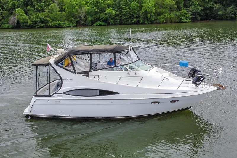 Slide: The Image of 2002 Carver 350 Mariner yacht cruising on a serene lake with lush green surroundings. - 1
