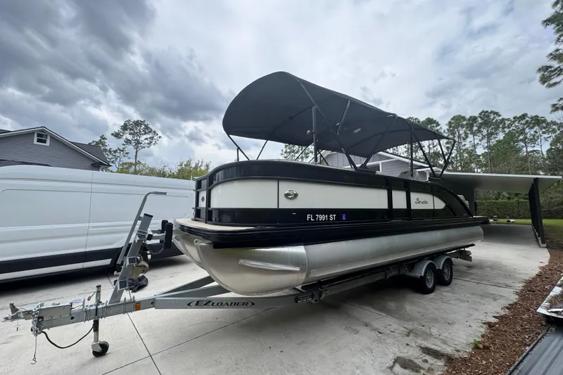 Slide: The Image of 2019 Barletta L25UCL pontoon boat on trailer, parked in driveway under cloudy sky. - 4