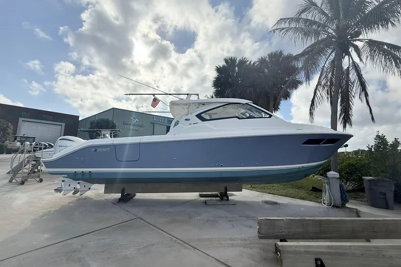 The Image of 2022 Pursuit DC 365 Dual Console boat on display, surrounded by palm trees and a cloudy sky. - 1
