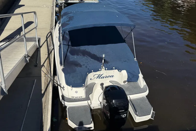 Slide: The Image of 2014 Sea Ray 220 Sundeck boat docked with blue cover and outboard motor. - 21