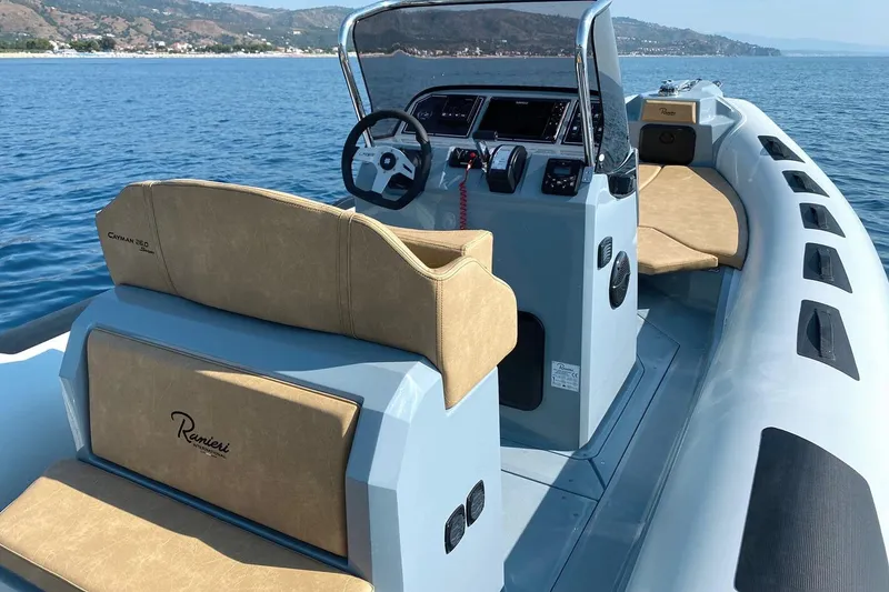 Slide: The Image of 2026 Ranieri Cayman 26.0 Sport boat interior with tan seating, steering console, and ocean backdrop. - 6