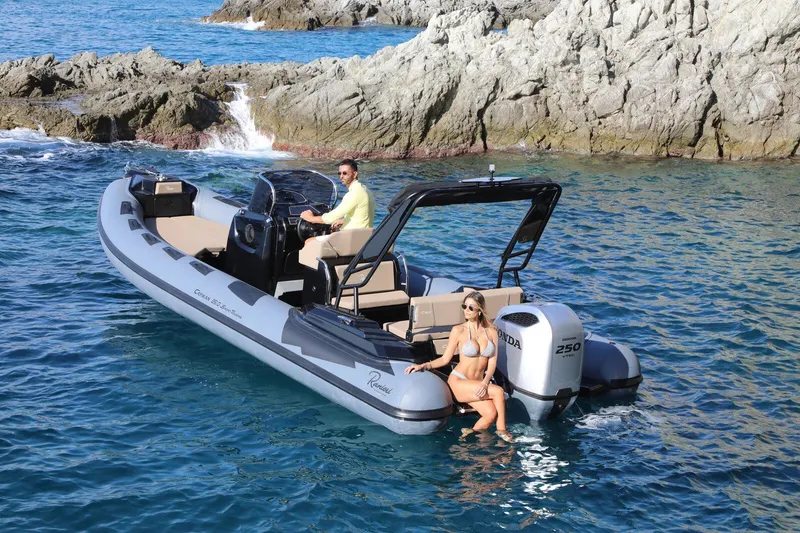 Slide: The Image of 2026 Ranieri Cayman 26.0 Sport Touring boat on clear blue water near rocky shore. - 5