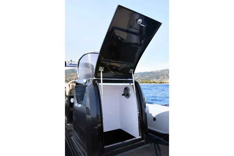 Slide: The Image of 2026 Ranieri Cayman 26.0 Sport Touring boat with open storage compartment by the sea. - 8