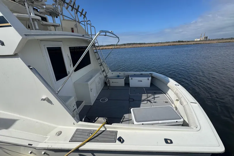 Slide: The Image of 1990 Hatteras 52 Convertible yacht deck with fishing gear, docked on calm water. - 18