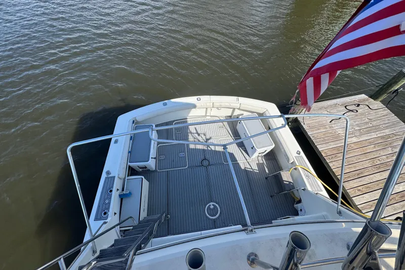 Slide: The Image of 1990 Hatteras 52 Convertible yacht deck with American flag, docked by wooden pier. - 2