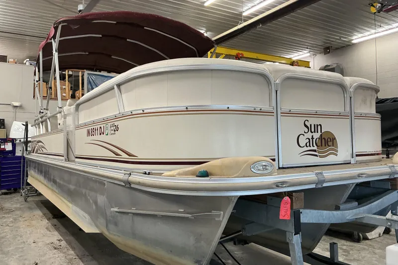 The Image of 2008 SunCatcher LX3 26 DC pontoon boat in indoor storage, featuring a maroon canopy. - 1